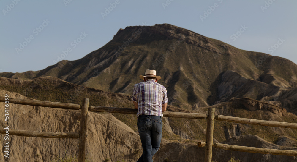 Rear view of adult man in hat on desert against mountain and sky. Almeria, Spain