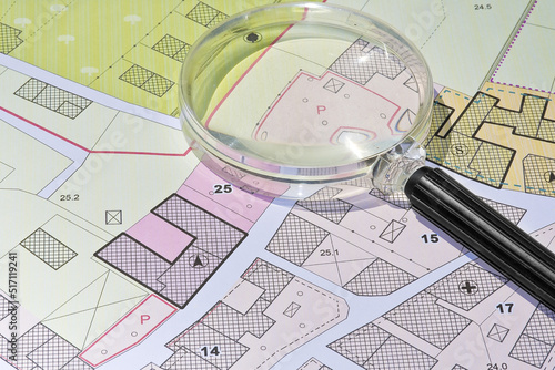 Imaginary cadastral map with buildings, land parcel and vacant plot - property registry and real estate concept seen through a magnifying glass
