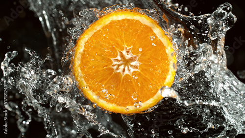 Slice of orange with water splashes on black background.