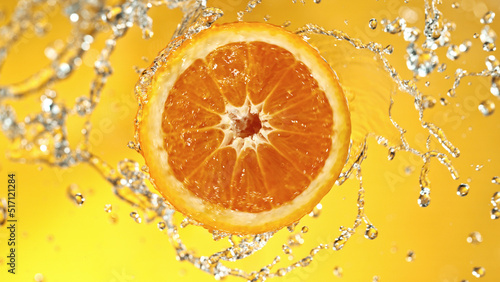 Slice of orange with water splashes on colored background.