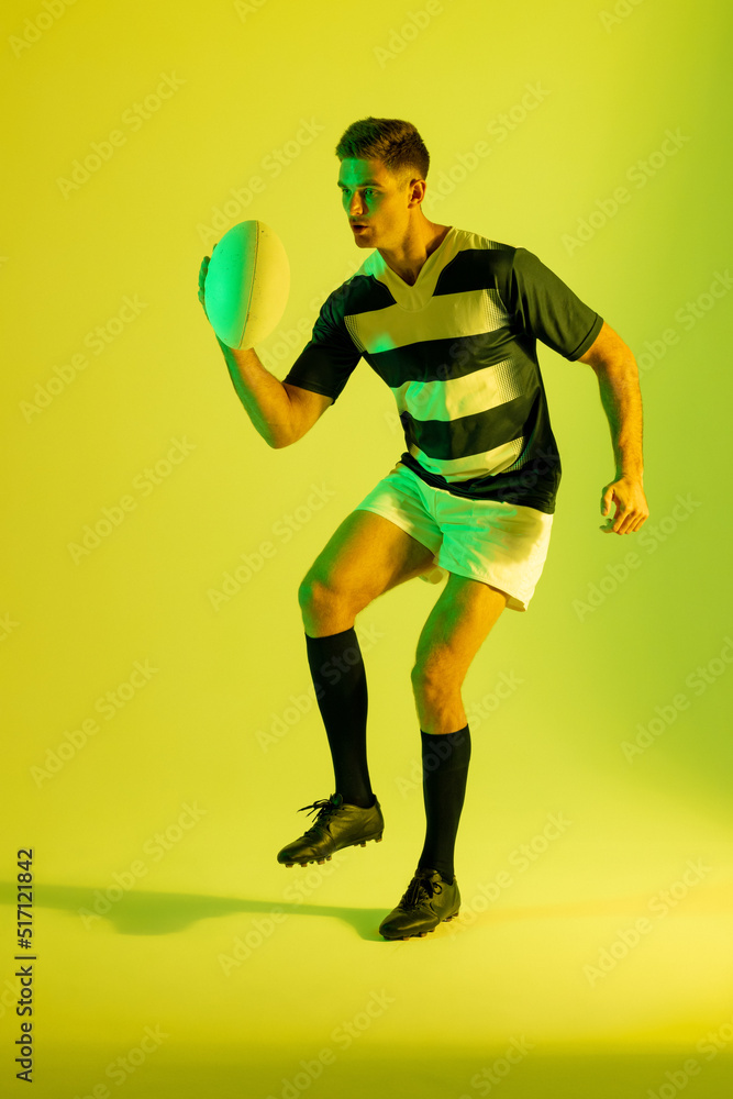 Caucasian male rugby player with rugby ball over yellow lighting Caucasian male rugby player with rugby ball over yellow lighting