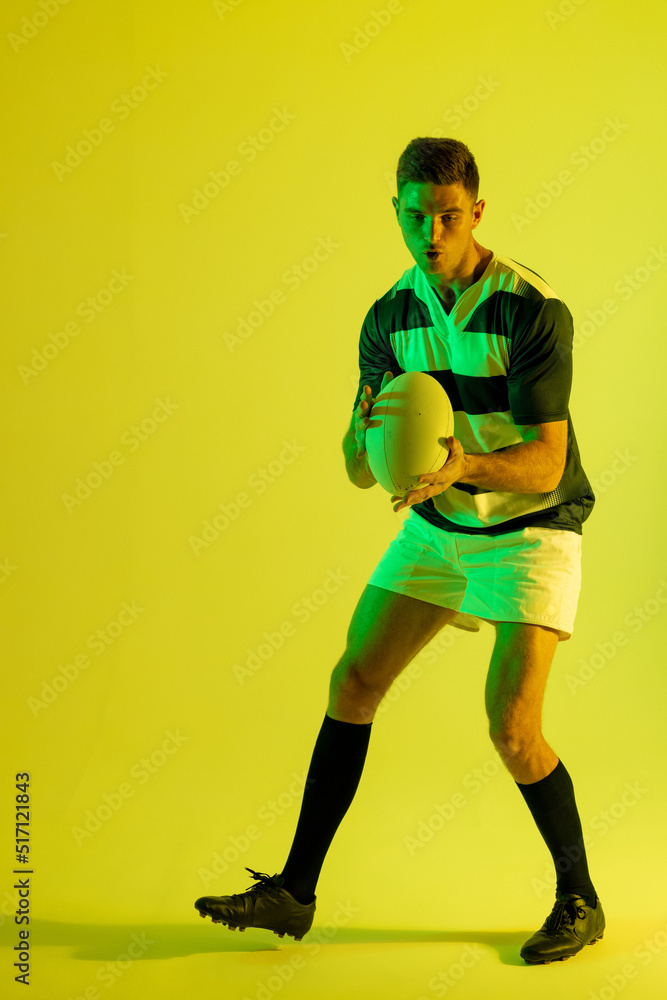 Caucasian male rugby player catching rugby ball over yellow lighting Caucasian male rugby player catching rugby ball over yellow lighting