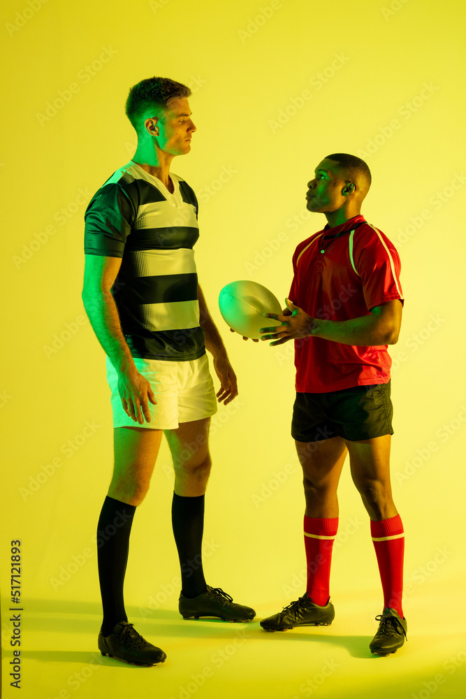 Diverse male rugby players with rugby ball over yellow lighting Diverse male rugby players with rugby ball over yellow lighting
