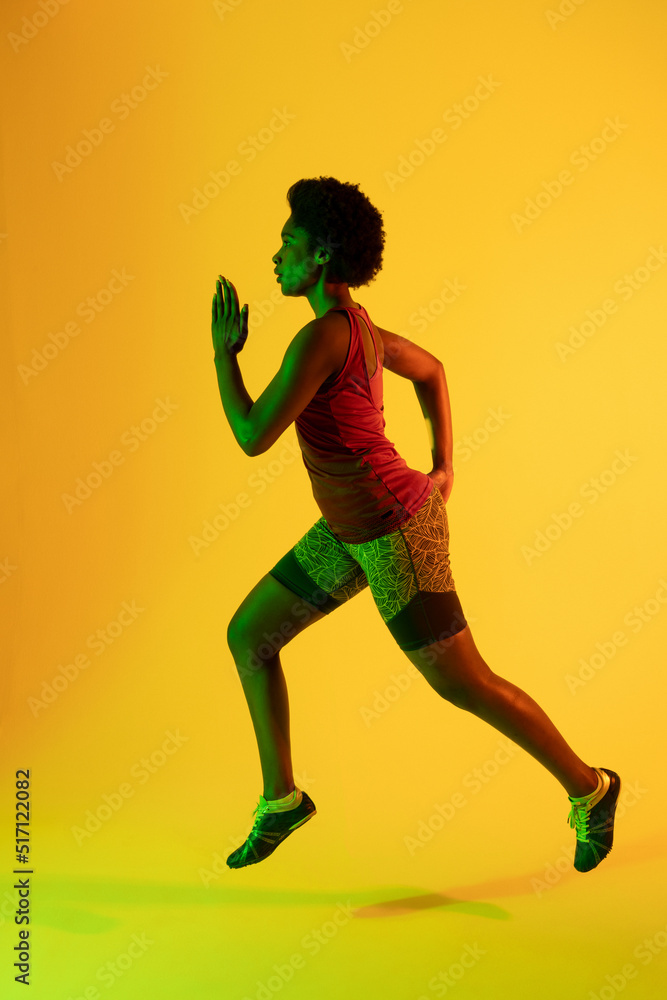 Vertical image of african american female athlete running in yellow lighting