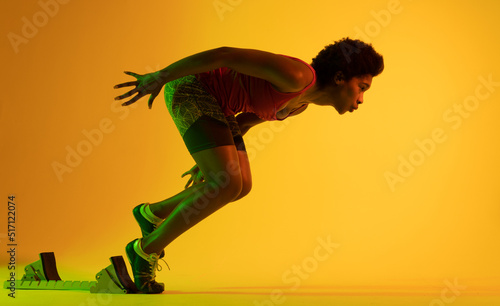 Image of african american female athlete preparing for run in yellow lighting