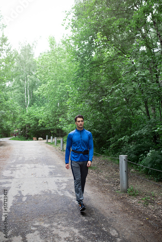 Sporty man in blue sportswear walking on the road close to the forest after jogging © Vitaliy