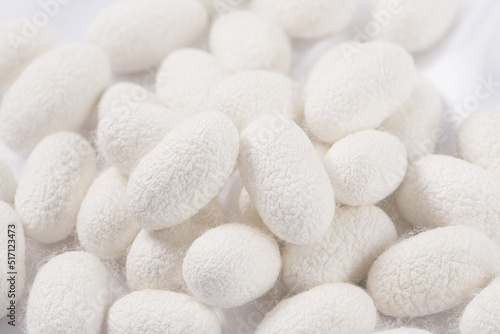Natural silkworm cocoons on white silk fabric background photo