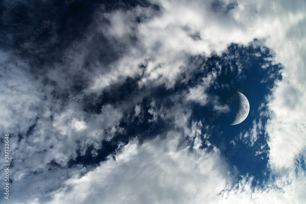 Dark blue dramatic sky background with white clouds and moon. Beautiful atmospheric cloud scape. Cumulus clouds.