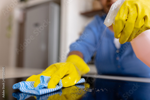 Midsection of biracial mature woman spraying disinfection on kitchen counter and cleaning with rag photo