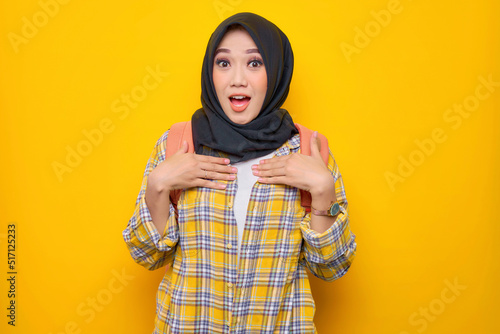 Shocked young Asian Muslim woman student in casual clothes and backpack, pointing at herself, feeling puzzled about something isolated on yellow background.Education school university college concept