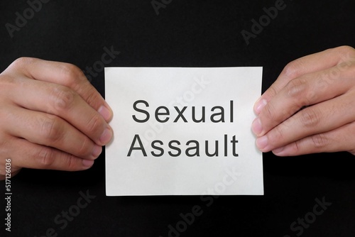 Obraz na płótnie Sexual assault crime or rape mug shot concept. Criminal hands holding paper placard with written word in dark black background. w salonie