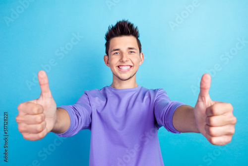 Young handsome man standing isolated blue background doing thumbs up gesture approving expression showing success. © Tetiana
