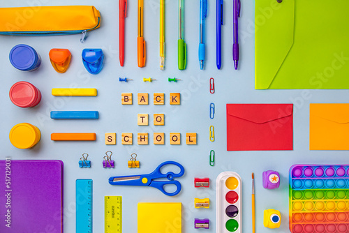 The inscription on the wooden squares in English letters is Back to school. Office supplies of bright colors are laid out around in order on a blue background
