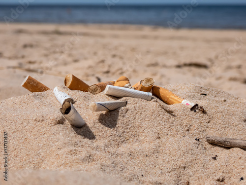 Cigarette butts in the white sand on Baltic sea beach as toxic plastic pollution in the beach sand. Most littered plastic item in the world. Beach pollution photo