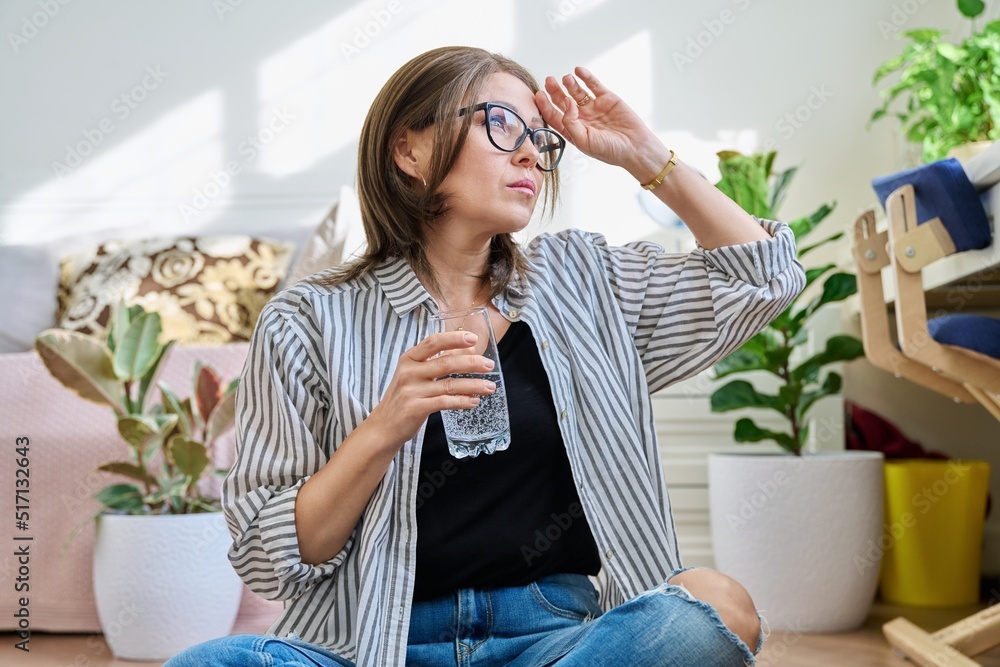 Mature woman suffering from headache, at home with a glass of water Mature woman suffering from headache, at home with a glass of water