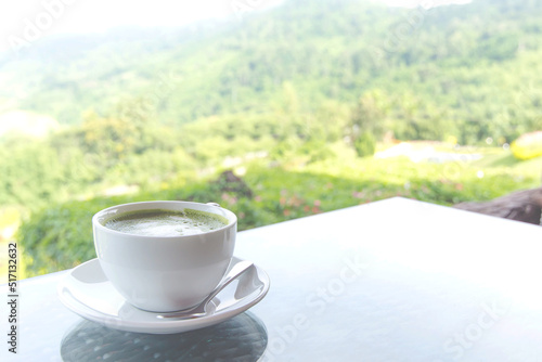 Green tea latte in a white cup on the natural hill background.