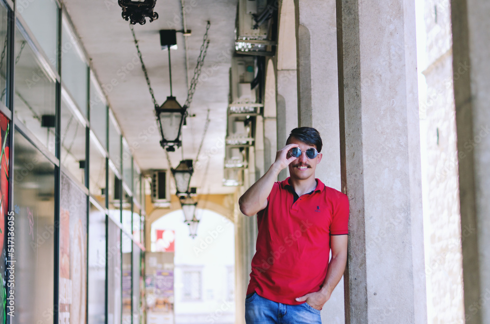 Young happy handsome bearded man, tourist walking in old city of Koper. Summer vacation. Sunglasses. Lifestyle portrait