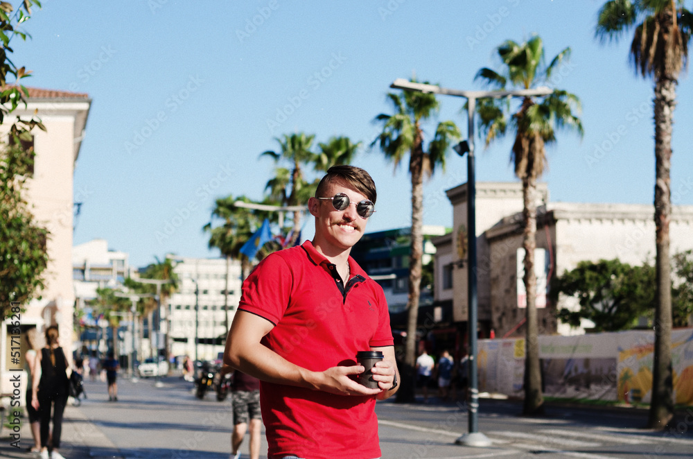 Young happy handsome bearded man, tourist walking in old city of Koper. drinking coffee. Summer vacation. palms. Sunglasses. Lifestyle 