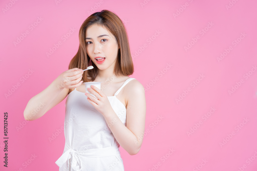 Image of young Asian woman eating yogurt on pink background Image of young Asian woman eating yogurt on pink background