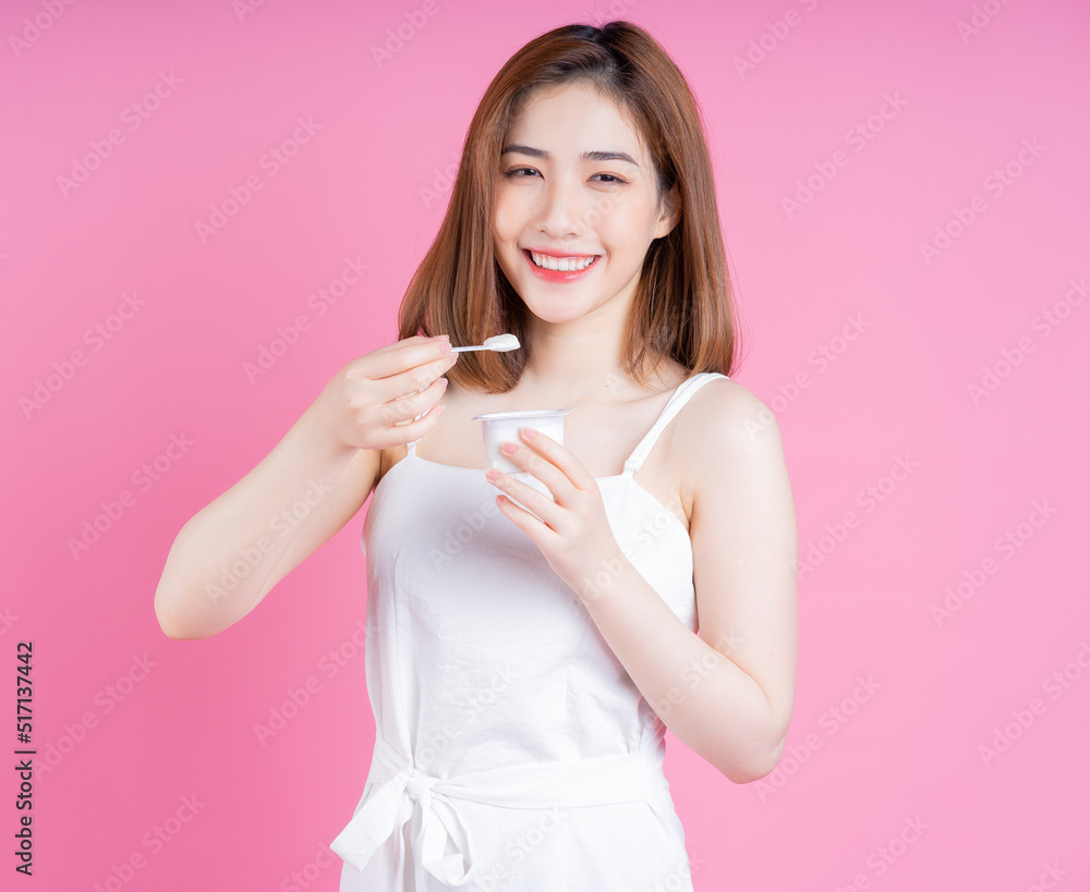 Image of young Asian woman eating yogurt on pink background Image of young Asian woman eating yogurt on pink background