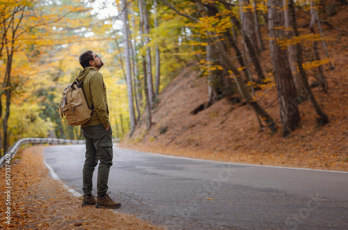 Young handsome man posing in autumn forest on road. young hipster guy with backpack , traveller standing in woods, Hiking, Forest, Journey, active healthy lifestyle, adventure, vacation concept. © YURII Seleznov