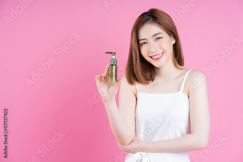 Image of young Asian woman holding spray bottle on pink background