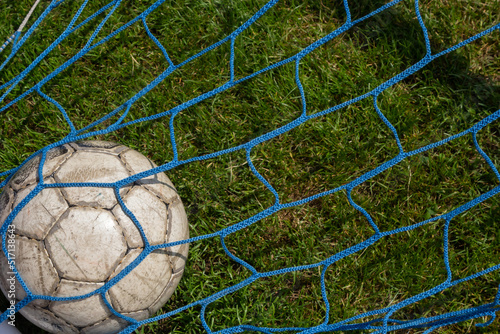 Fototapeta Naklejka Na Ścianę i Meble -  old soccer ball in the net on the background of grass soccer field. Summer sunny day