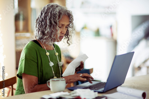 Senior woman with receipts banking at laptop
