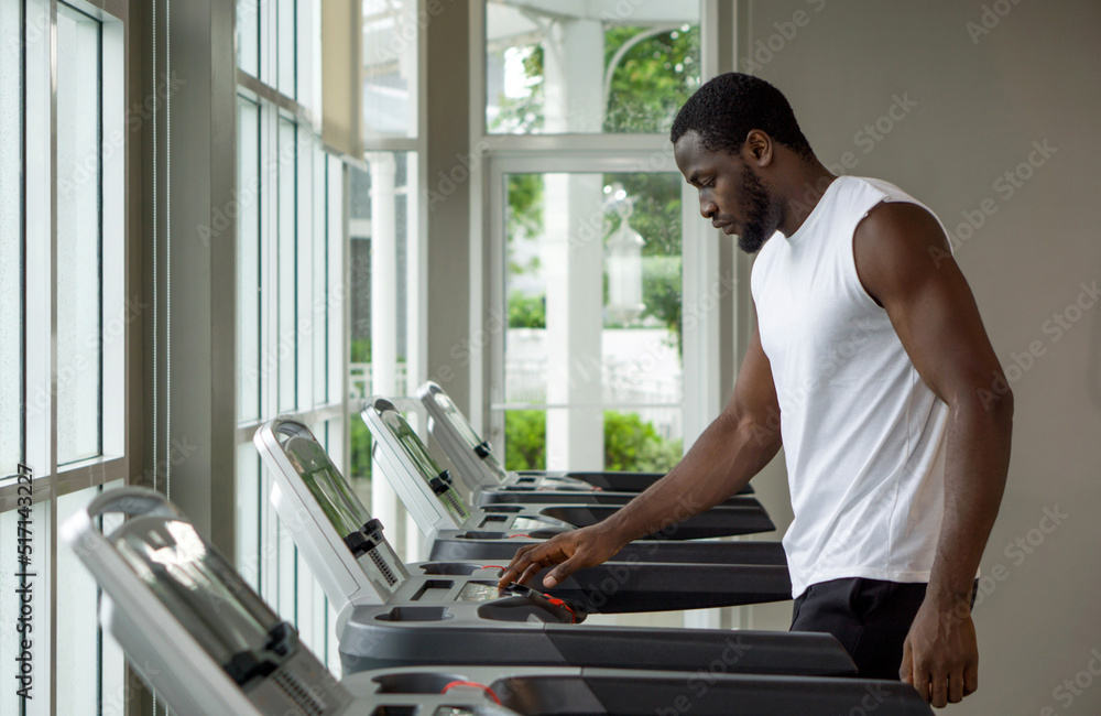 Fototapeta premium Young short curly black hair man with moustache and beard selecting running program on treadmill in the gym.