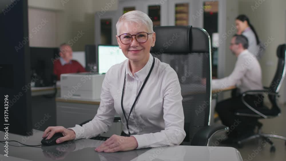 Senior woman executive smiling at camera sitting at desk in modern office Senior woman executive smiling at camera sitting at desk in modern office