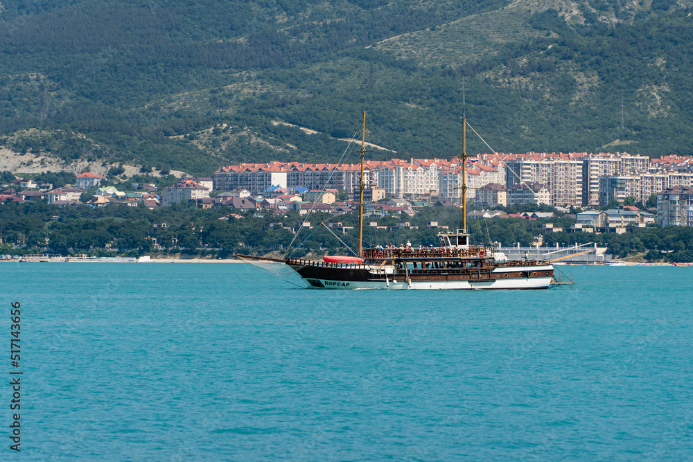 Two-masted pleasure yacht with Corsair engine sails along shore Gelendzhik Bay. Blurred background.. People on deck of  yacht. Inscription 