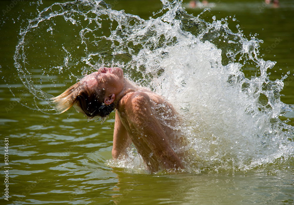 boy having fun in water of forest lake in summer sunny day with splash