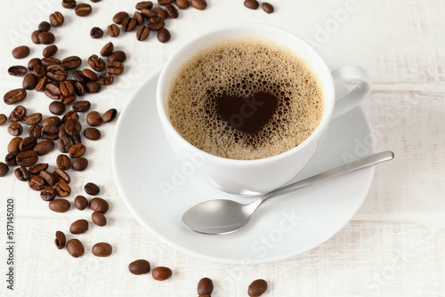 Cup of coffee with heart pattern and coffee beans on white wooden table Top view
