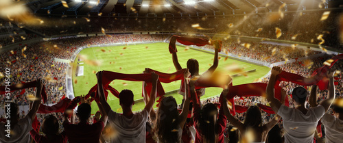 Back view of football, soccer fans cheering their team with colorful scarfs at crowded stadium at evening time. Concept of sport, support, competition. Out of focus effect © master1305
