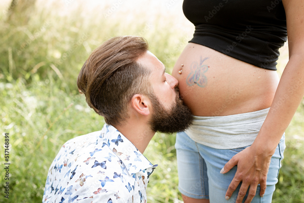 Man with beard draws butterfly on belly of his pregnant girlfriend on a meadow outside in nature Man with beard draws butterfly on belly of his pregnant girlfriend on a meadow outside in nature