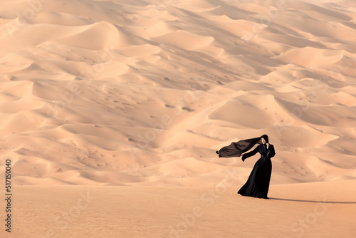 Young woman in a traditional emirati abaya in the desert. Liwa desert, Abu Dhabi, UAE. photo