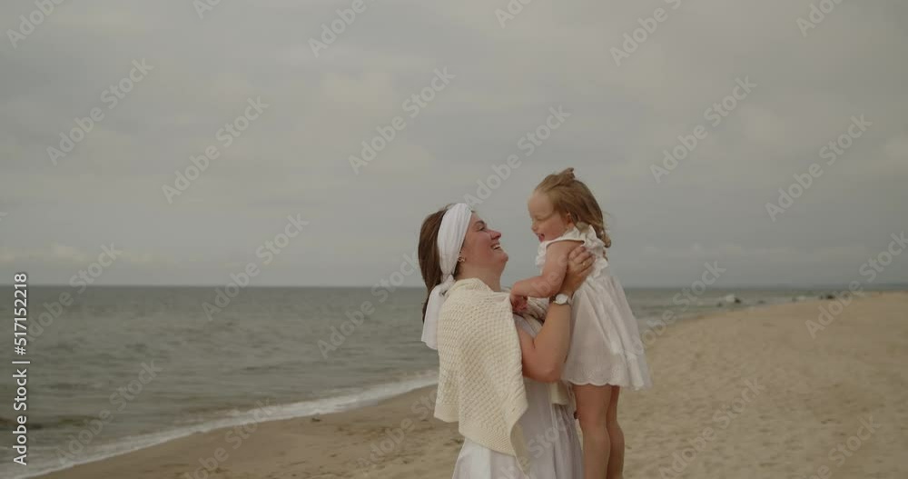 Young mother and baby daughter spend time on the beach together. Mom and toddler cute little girl have fun fooling around and spinning by the sea. Motherhood, maternity, single mother, family concept. Young mother and baby daughter spend time on the beach together. Mom and toddler cute little girl have fun fooling around and spinning by the sea. Motherhood, maternity, single mother, family concept.