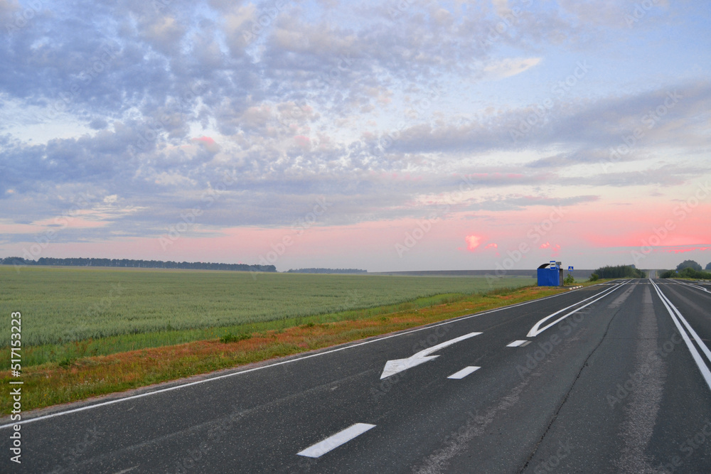 Bus stop next to the Gray paved road at dawn in the field Bus stop next to the Gray paved road at dawn in the field