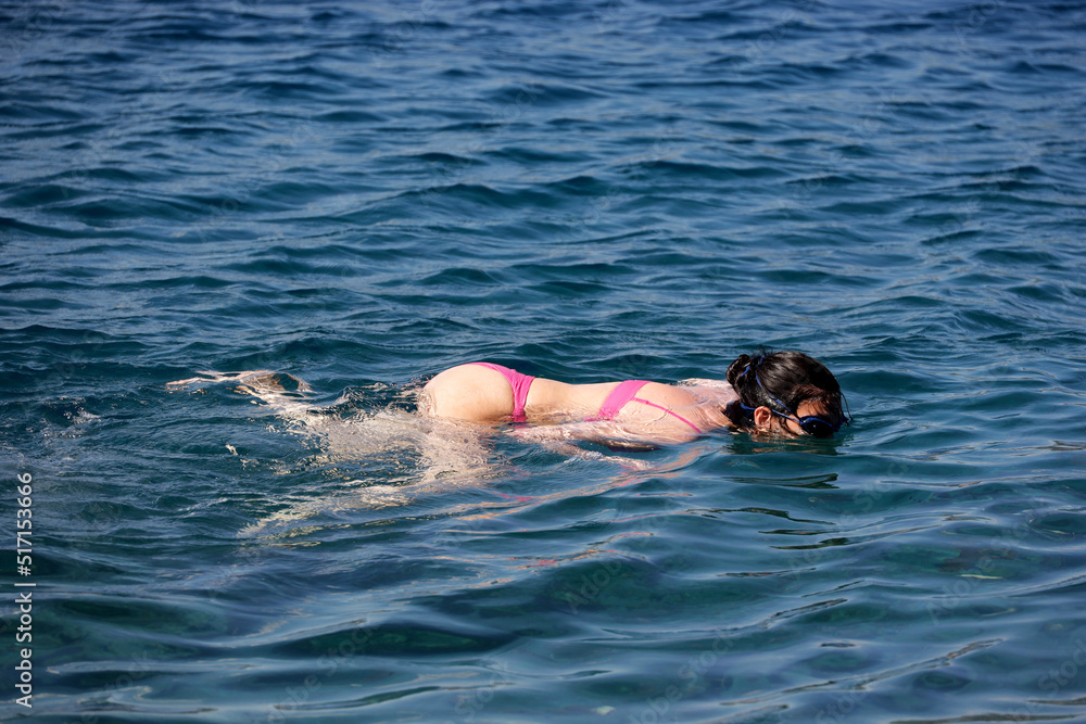 Snorkeling in a sea, girl in bikini swimming in diving glasses in transparent water. Beach vacation in summer