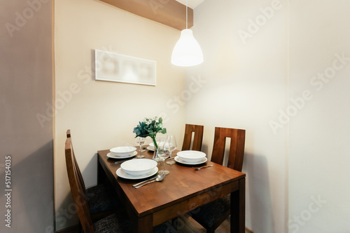 Room with set dining table and four chairs.  Table and chairs are made of solid wood.  On the table is dining set consisting of plates, cutlery and wine glasses. In addition there is also a flower.