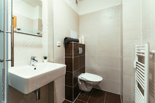 A small modern bathroom with a large square sink and toilet.  The tiling in the bathroom is two-tone  consisting of brown and beige tiles. There are also some additional items as towel  candles  etc.