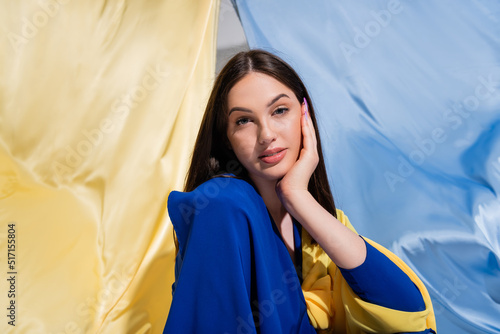 pretty ukrainian woman in stylish color block clothing posing near blue and yellow flag.