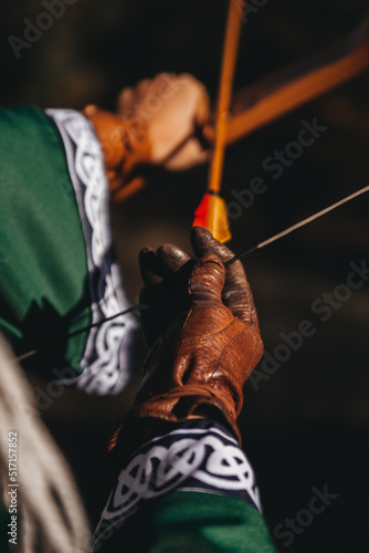 Close-up: Woman's hand in leather glove draws arrow on bow, aiming, medieval theme