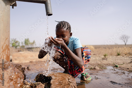 Little African girl splashing herself with copious amounts of clean water at a freshwater well located in an Sub saharan arid region photo