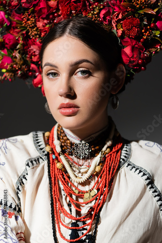 portrait of brunette and young ukrainan woman in floral wreath with red berries isolated on dark grey.