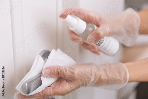 Cleaning door handles with wet wipe and white gloves. Sanitize surfaces prevention in hospital and public spaces against corona virus. Woman hand using towel for cleaning home room door link.