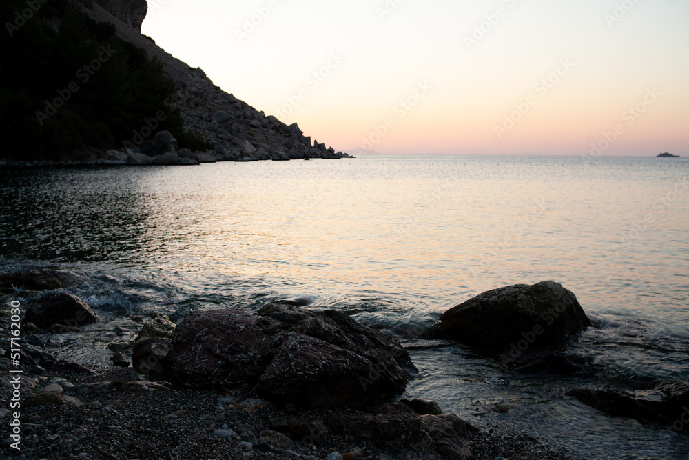 Sunrise over mountain rock in sea water. Sunrise seascape in calm sea. Rocks silhouette and golden reflections on the rippled water Sunrise over mountain rock in sea water. Sunrise seascape in calm sea. Rocks silhouette and golden reflections on the rippled water