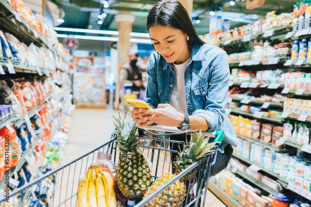 Obraz premium Happy young woman shopping for groceries in supermarket