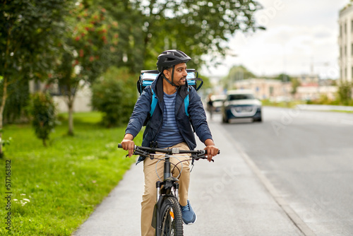 food shipping, transportation and people concept - happy smiling delivery man in bike helmet with thermal insulated bag riding bicycle on city street © Syda Productions