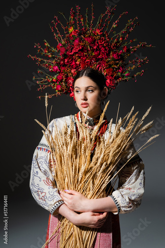 ukrainan woman in floral wreath with red berries holding wheat spikelets on dark grey.